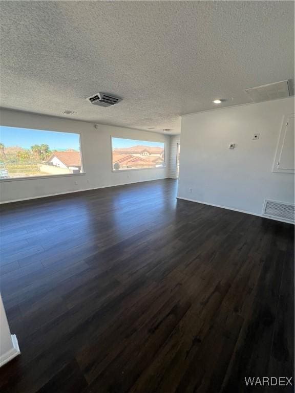 unfurnished living room with a textured ceiling, dark wood finished floors, and visible vents