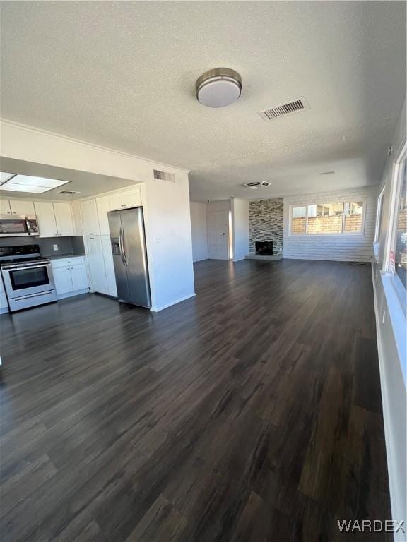 unfurnished living room featuring visible vents, dark wood-style flooring, a textured ceiling, and a stone fireplace