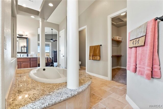 ensuite bathroom featuring stone tile floors, a ceiling fan, vanity, ensuite bath, and baseboards