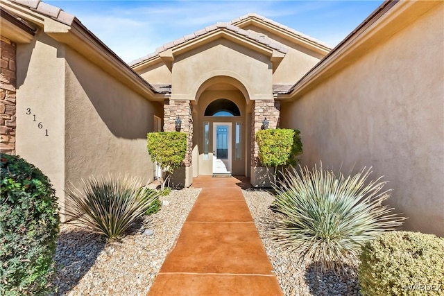 view of exterior entry featuring stone siding, a tiled roof, and stucco siding