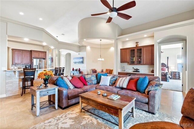 living room featuring arched walkways, decorative columns, light tile patterned floors, a ceiling fan, and vaulted ceiling