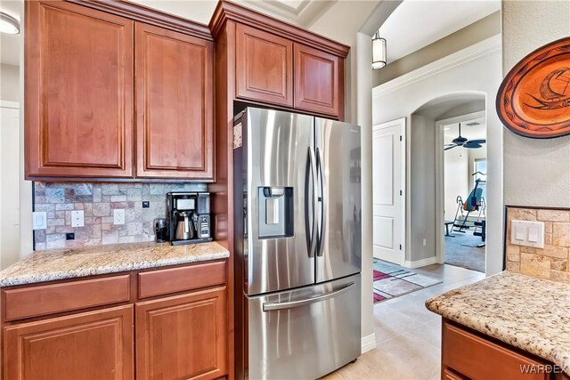 kitchen featuring arched walkways, ceiling fan, light stone countertops, stainless steel refrigerator with ice dispenser, and decorative backsplash