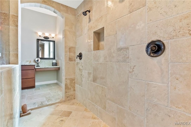 full bathroom with stone finish flooring, tiled shower, and vanity