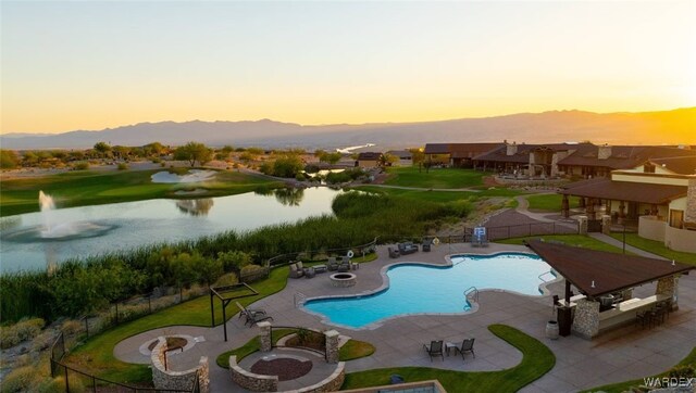 pool at dusk with a residential view, a water view, a community pool, fence, and a patio area