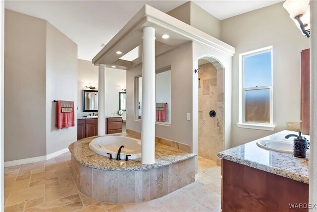 full bathroom featuring baseboards, two vanities, a sink, ornate columns, and a bath