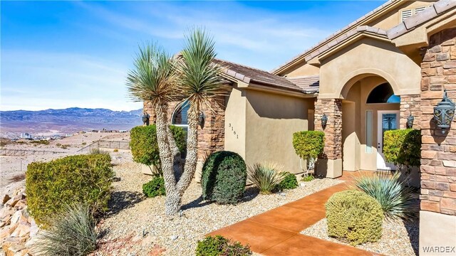 property entrance with stone siding, a tiled roof, a mountain view, and stucco siding