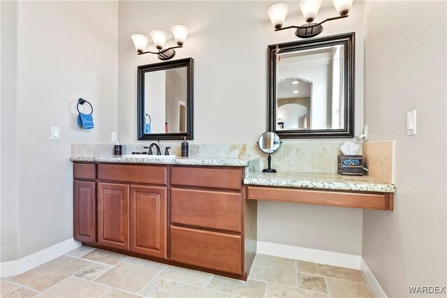 bathroom with stone finish floor, an inviting chandelier, vanity, and baseboards