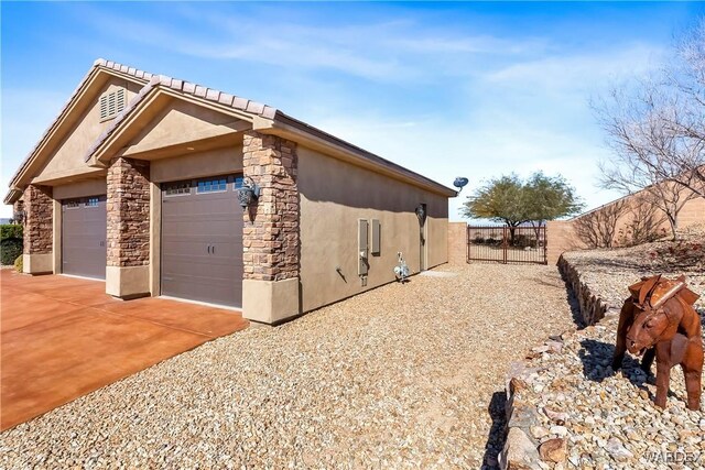 view of side of property featuring an attached garage, fence, stone siding, driveway, and stucco siding