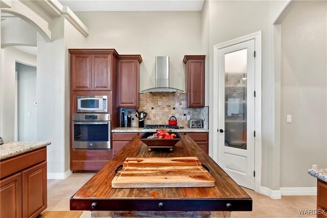 kitchen featuring stainless steel appliances, wall chimney range hood, a kitchen island, and wood counters