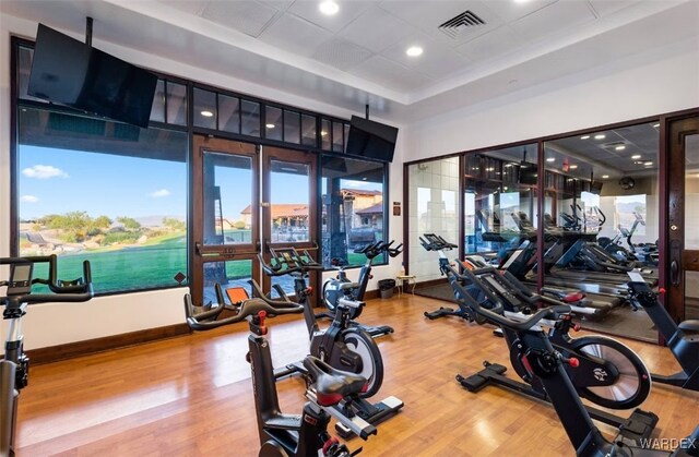 exercise room with wood finished floors, visible vents, and baseboards