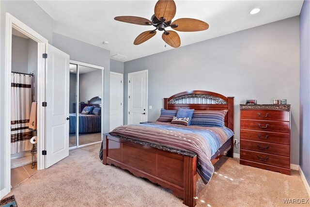 bedroom featuring a ceiling fan, a closet, light colored carpet, and ensuite bath