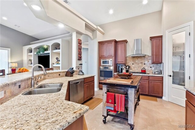 kitchen featuring stainless steel appliances, a sink, wooden counters, wall chimney range hood, and a center island