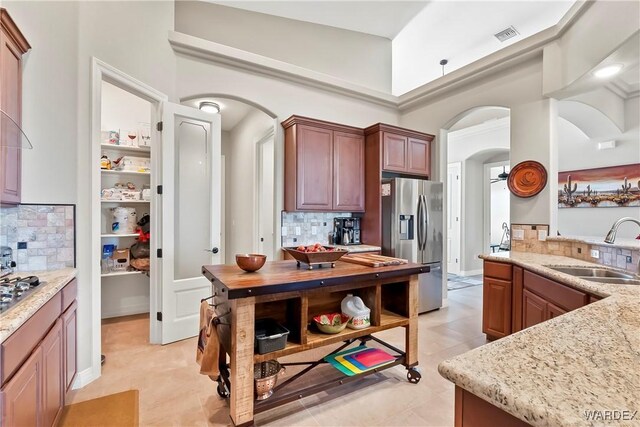 kitchen with stainless steel appliances, arched walkways, a sink, and light stone countertops