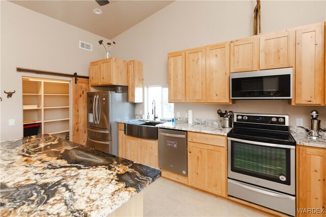 kitchen with stainless steel appliances, light brown cabinets, light stone counters, and a barn door