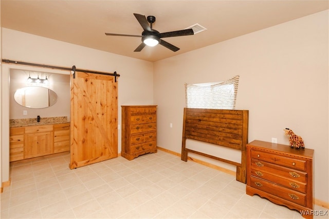 bedroom featuring ensuite bathroom, a barn door, a sink, a ceiling fan, and baseboards