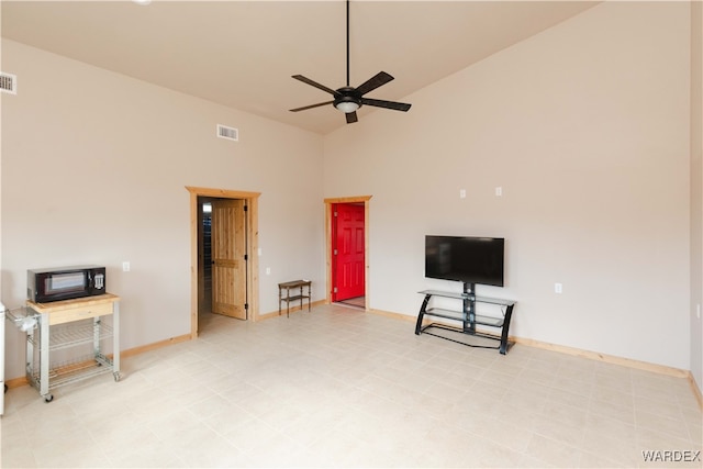 living area with baseboards, a towering ceiling, visible vents, and a ceiling fan