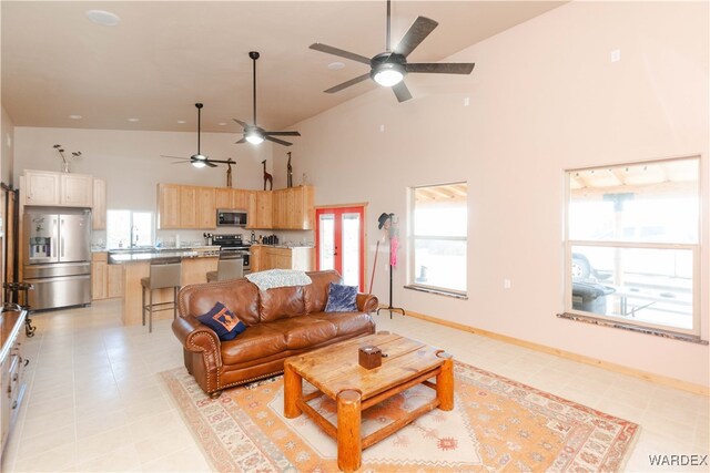 living area featuring high vaulted ceiling, baseboards, a healthy amount of sunlight, and light floors