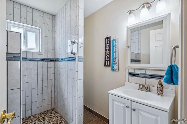 bathroom featuring tile patterned flooring, vanity, baseboards, tiled shower, and tasteful backsplash