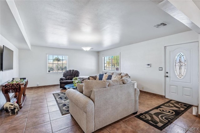 tiled living room featuring a healthy amount of sunlight, visible vents, a textured ceiling, and baseboards