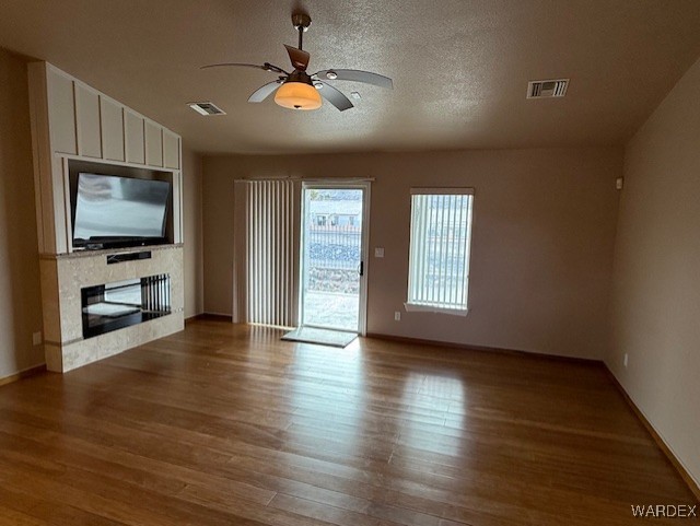 unfurnished living room featuring wood finished floors, a glass covered fireplace, and visible vents