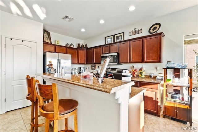 kitchen featuring stainless steel appliances, visible vents, a kitchen island, light stone countertops, and a kitchen breakfast bar