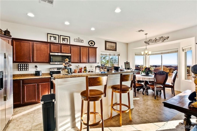 kitchen with light stone counters, a kitchen island, a kitchen breakfast bar, hanging light fixtures, and appliances with stainless steel finishes