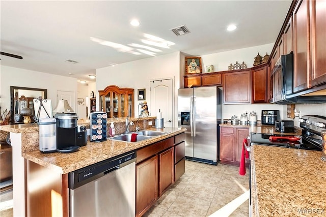 kitchen with light stone counters, stainless steel appliances, a sink, a kitchen breakfast bar, and an island with sink