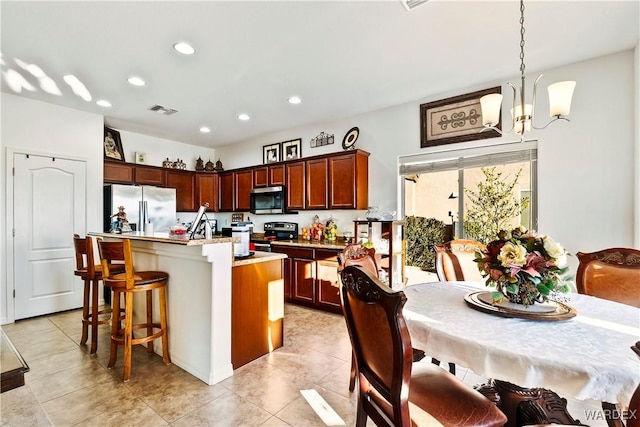 kitchen with decorative light fixtures, a notable chandelier, stainless steel appliances, visible vents, and a kitchen island with sink