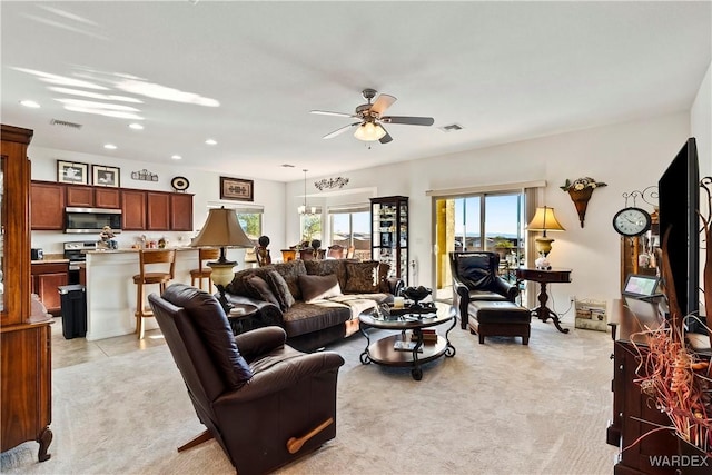 living room featuring light carpet, visible vents, and ceiling fan with notable chandelier