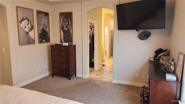 bedroom featuring arched walkways, baseboards, a walk in closet, and light colored carpet