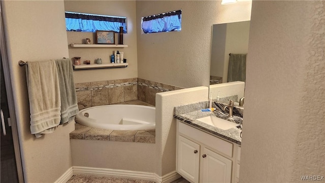 full bath featuring a textured wall, a garden tub, and vanity