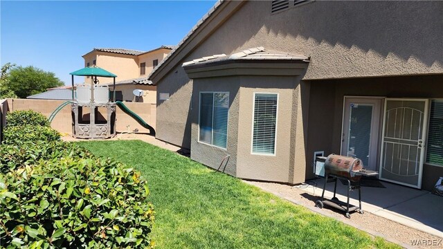 rear view of property featuring a tile roof, a playground, a lawn, and stucco siding