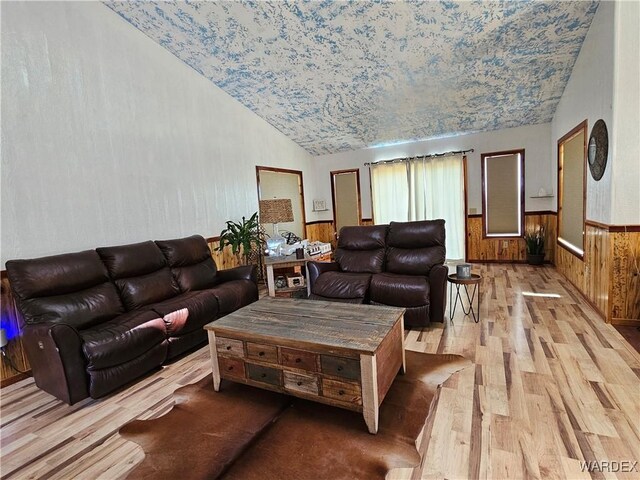 living room with wooden walls, light wood-type flooring, wainscoting, and lofted ceiling