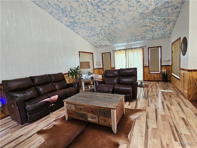 living room with wooden walls, light wood-type flooring, wainscoting, and lofted ceiling