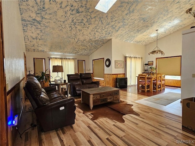 living room with vaulted ceiling with skylight, a wainscoted wall, and light wood finished floors
