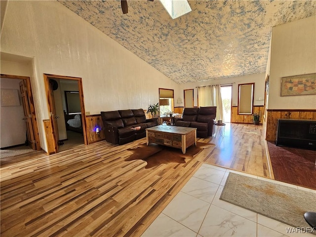 living room with a wainscoted wall, high vaulted ceiling, a fireplace with flush hearth, and marble finish floor