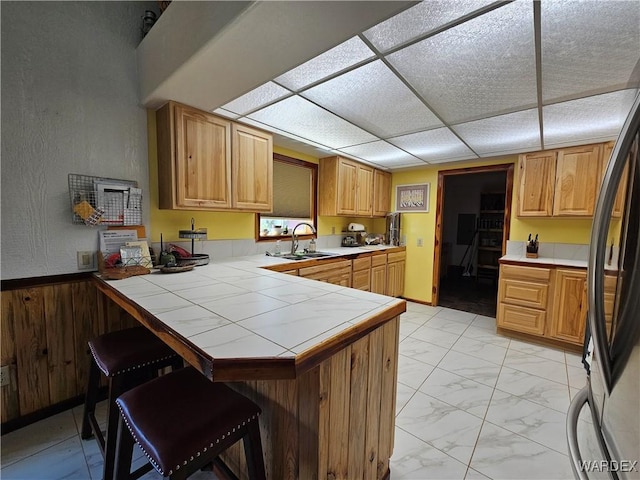 kitchen featuring a peninsula, a breakfast bar, a sink, marble finish floor, and freestanding refrigerator