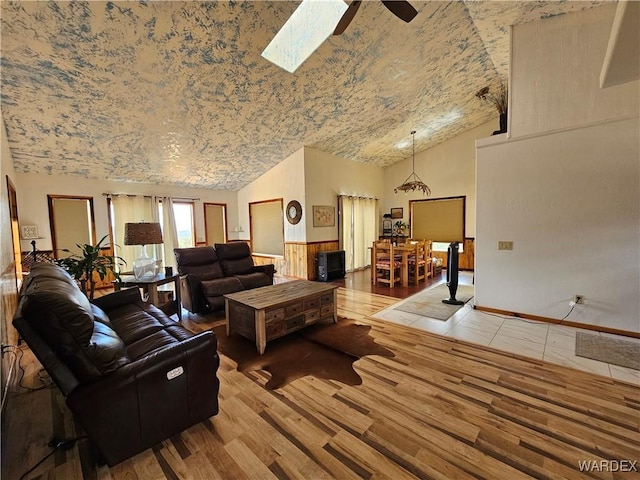 living room with light wood-style floors, a skylight, ceiling fan, and high vaulted ceiling