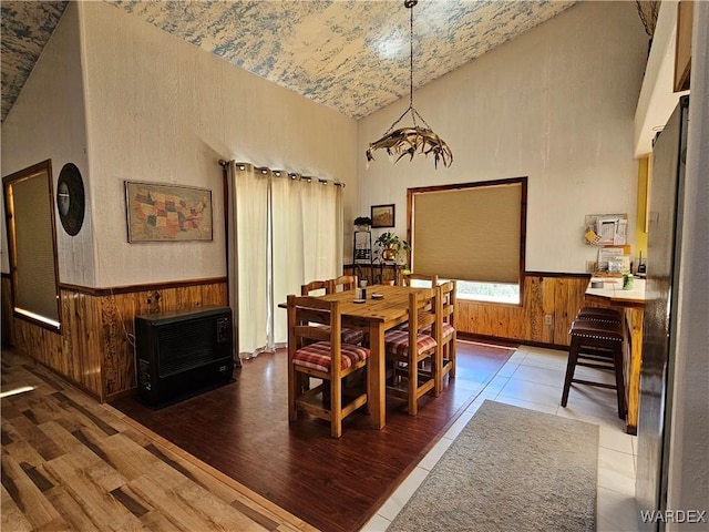 dining area with high vaulted ceiling, wood walls, wainscoting, and heating unit