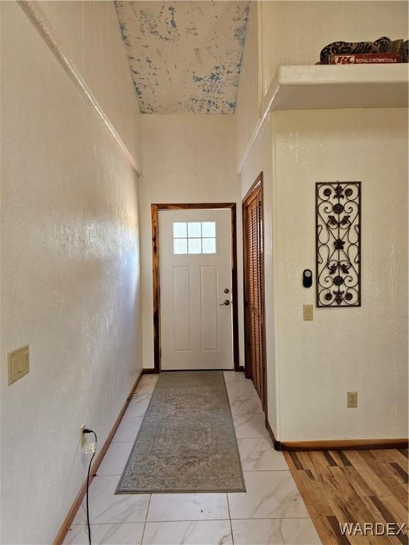 doorway featuring marble finish floor, a high ceiling, and baseboards