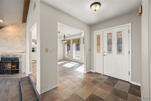 foyer entrance with beam ceiling, a tiled fireplace, visible vents, and baseboards