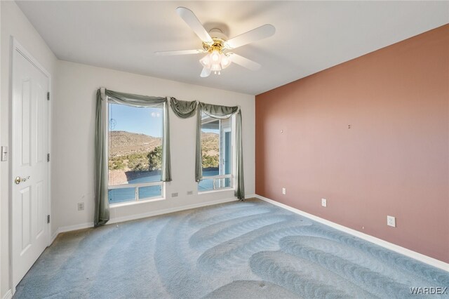 empty room with carpet floors, ceiling fan, baseboards, and a mountain view