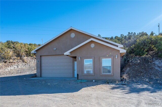 view of front of property featuring a garage, dirt driveway, and stucco siding