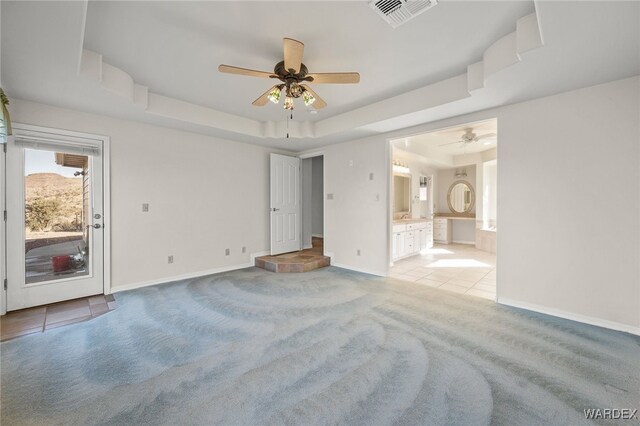 empty room featuring light tile patterned floors, light colored carpet, visible vents, baseboards, and a raised ceiling