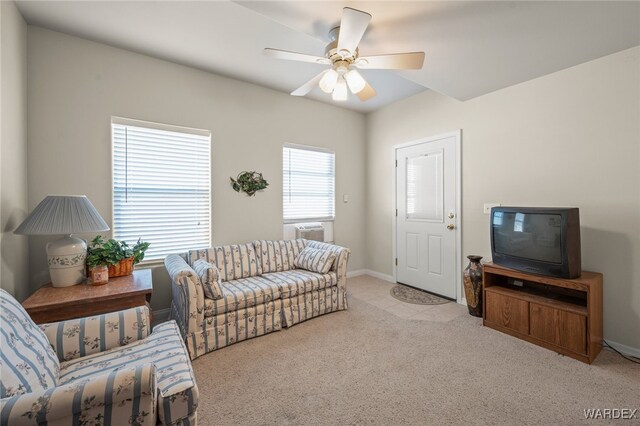 living area featuring baseboards, a ceiling fan, and light colored carpet