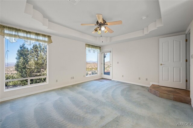 carpeted empty room with ceiling fan, visible vents, baseboards, and a raised ceiling