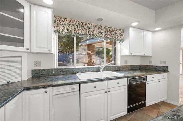 kitchen featuring dark stone counters, dishwasher, glass insert cabinets, white cabinetry, and a sink