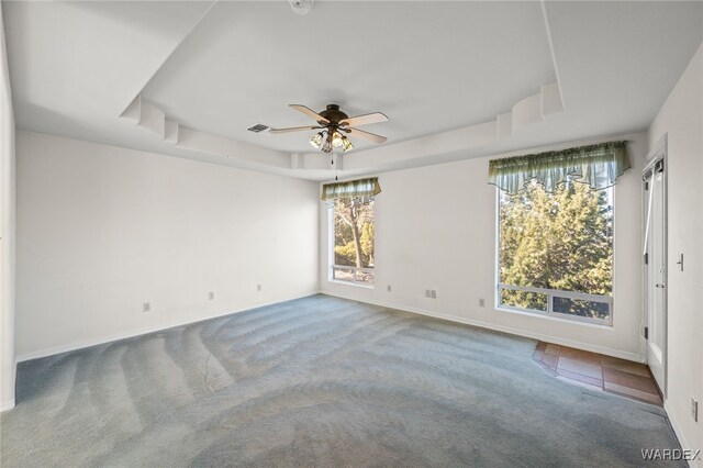 unfurnished room featuring ceiling fan, carpet floors, visible vents, baseboards, and a tray ceiling