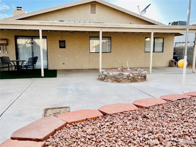 rear view of house featuring a fire pit, a chimney, a patio area, and stucco siding