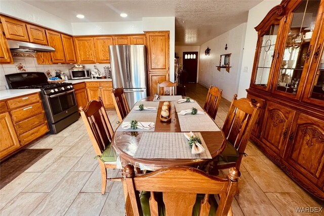 kitchen featuring tasteful backsplash, appliances with stainless steel finishes, brown cabinets, light countertops, and under cabinet range hood